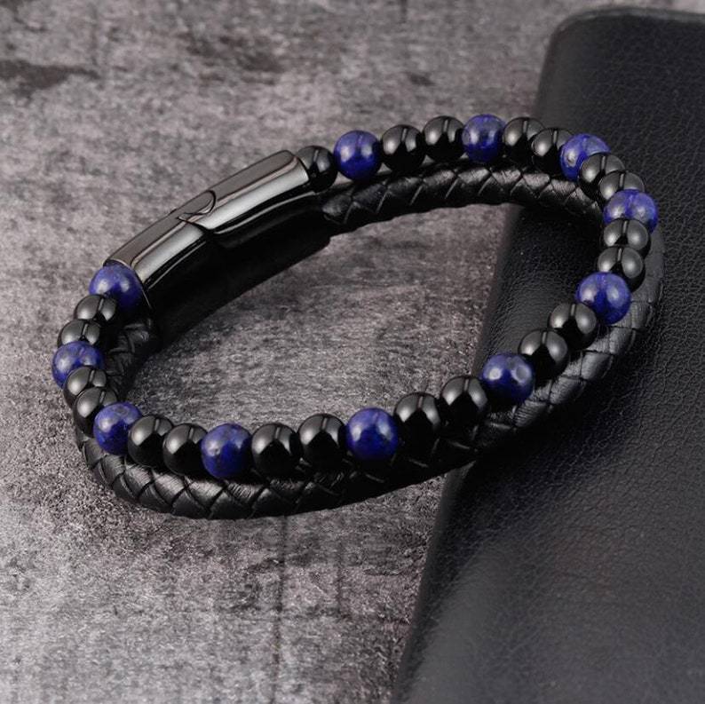 Black braided leather and blue beaded bracelet on a textured surface