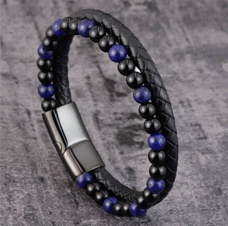 Black braided leather bracelet with blue beads on a gray textured background