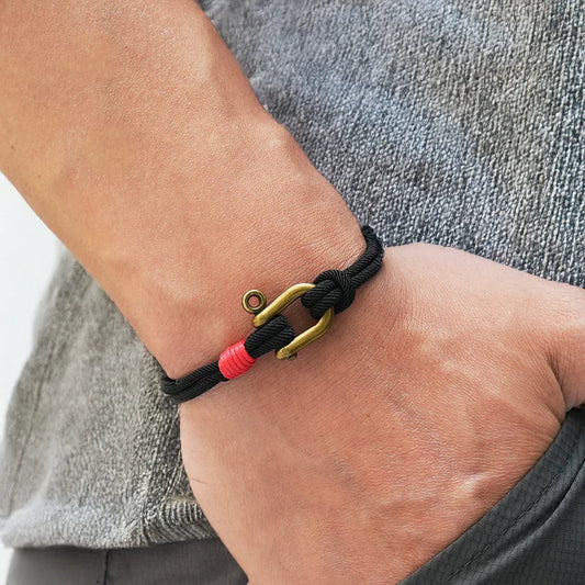 Bracelet with a gold clasp and pink bead on a wrist against a neutral background