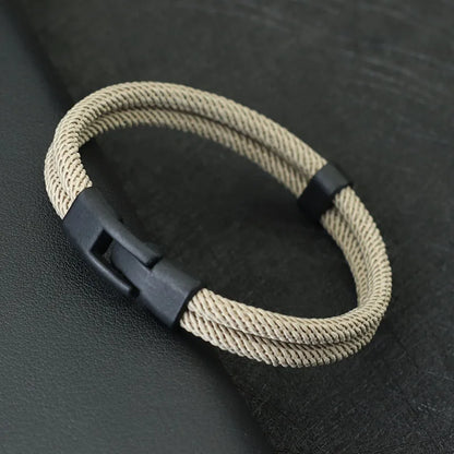 Beige braided bracelet with a black clasp on a dark textured surface