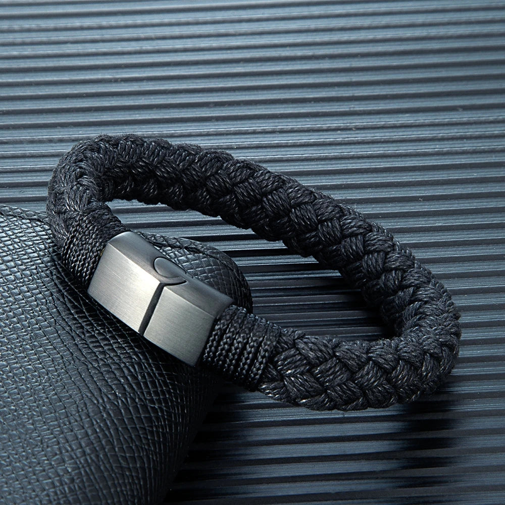 Black braided bracelet with a metallic clasp on a textured gray background