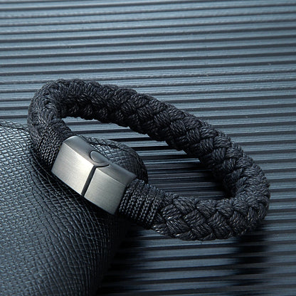 Black braided bracelet with a metallic clasp on a textured gray background
