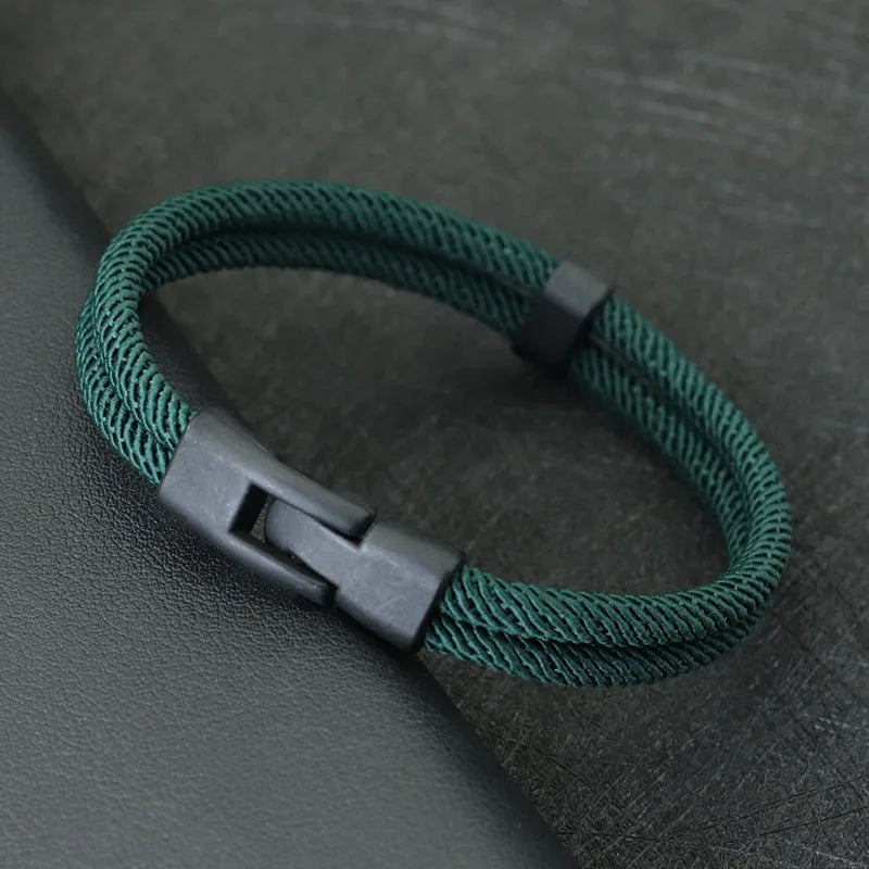 Green braided bracelet with a black clasp on a dark gray background
