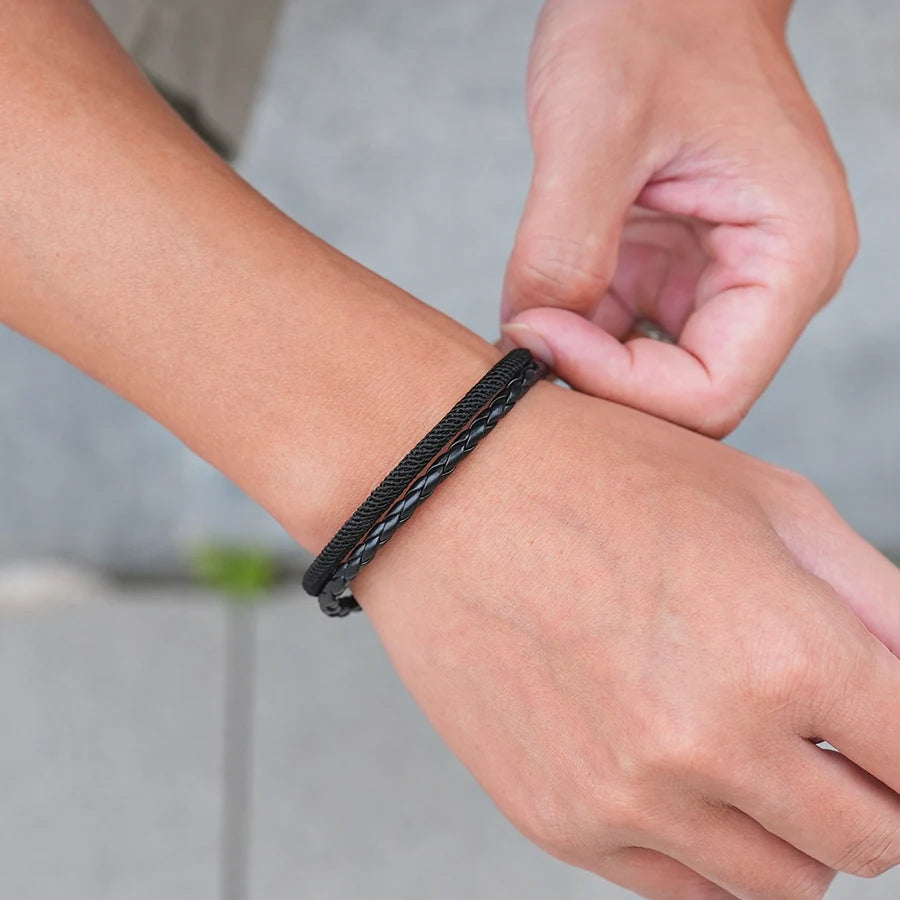 Person adjusting a black braided bracelet on their wrist with a blurred background